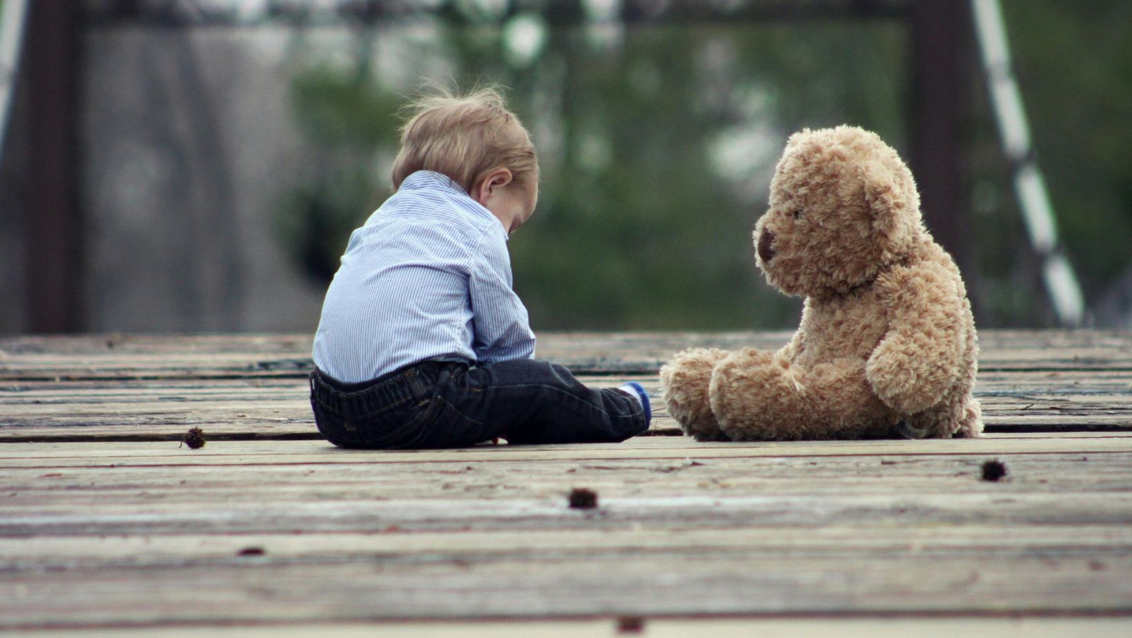 Little boy sitting with a brown teddy bear.